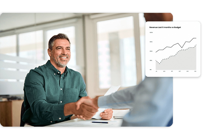 A man in a green shirt smiles and shakes hands with someone across a desk. There is a graph in the image showing an upward trend.